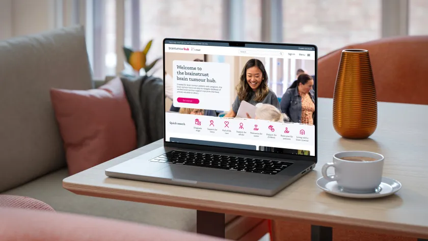 Laptop displaying the Brain Tumour Hub on a coffee table with cup and saucer.