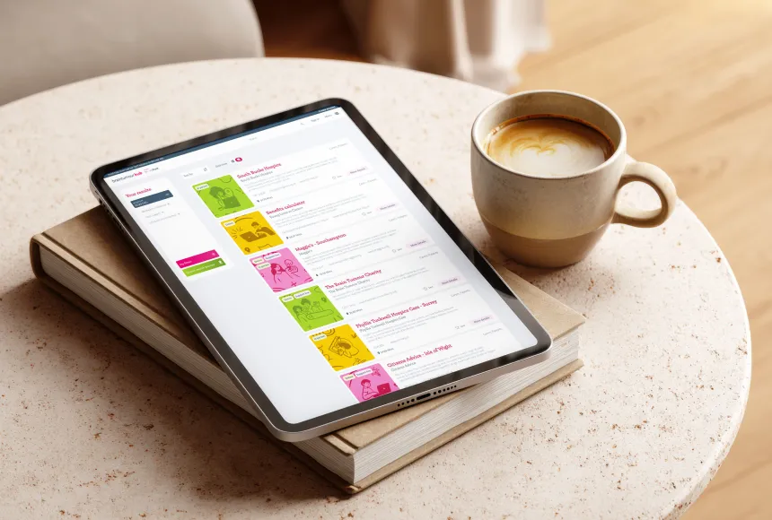 Tablet mockup of Brain Tumour Hub resources search page, laid on a coffee table and book.