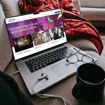 Culture connects website on laptop, on a sofa with headphones.