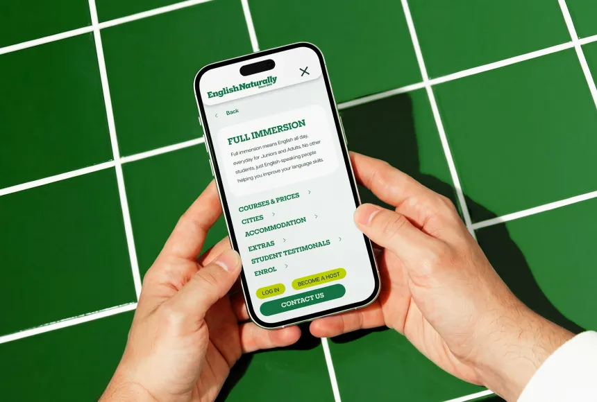 Smartphone displaying the English Naturally mobile navigation menu on a green tiled surface
