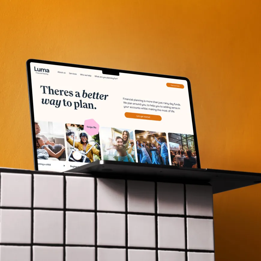 Laptop perched on the edge of a white tiled shelf against an orange background.